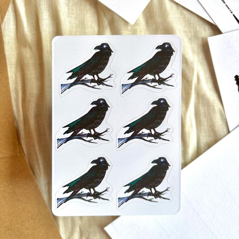 May include: A sheet of six stickers depicting a black raven on a branch. The raven has a blue eye and green wing accents. The stickers are on a white background.
