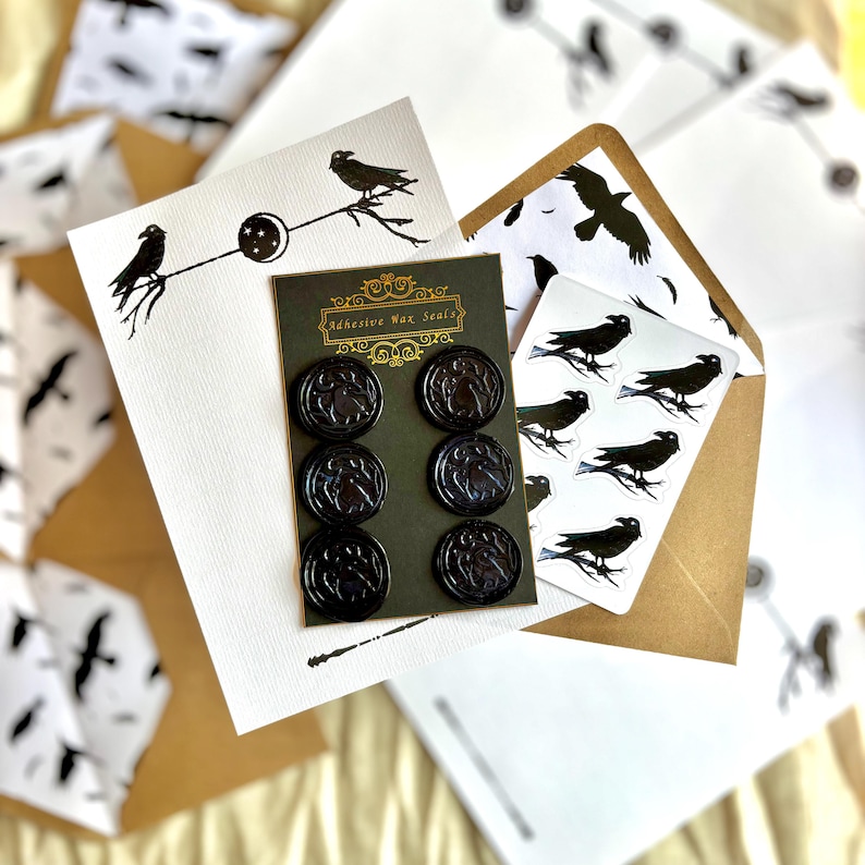 May include: A selection of raven-themed stationery. The image shows black wax seals, stickers, and cards adorned with raven and branch illustrations. The packaging displays the text "Adhesive Wax Seals".