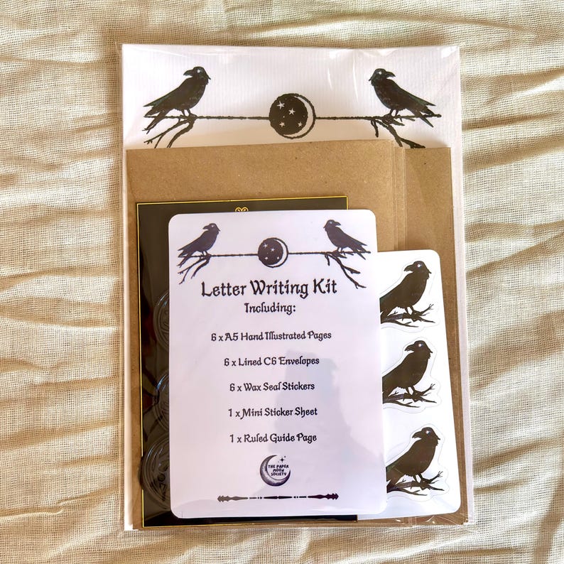May include: A letter writing kit featuring a raven and moon design. The kit includes 6 A5 illustrated pages, 6 C6 lined envelopes, wax seal stickers, a mini sticker sheet, and a ruled guide page. The kit is packaged in a clear wrapper.