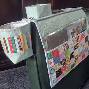 May include: A quilted sage green sofa armrest organizer featuring a patchwork pocket with multi-colored fabric squares, a cylindrical side cup holder with vertical striped fabric, and a small square top compartment with floral trim accents.