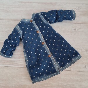 May include: A blue denim jacket with white polka dots and wooden buttons. The jacket has long sleeves and a button-up front. The garment is made of denim fabric and has a classic design.