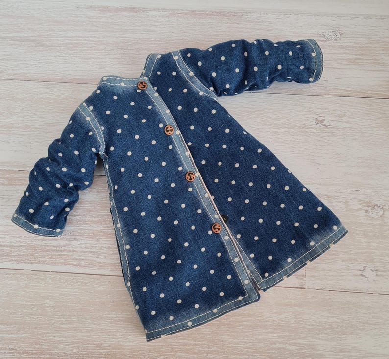 May include: A blue denim jacket with white polka dots and wooden buttons. The jacket has long sleeves and a button-up front. The garment is made of denim fabric and has a classic design.