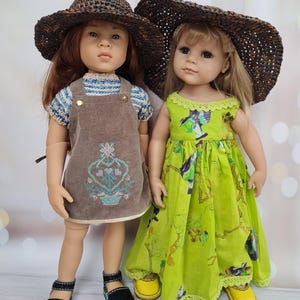 Könnte beinhalten: Zwei Puppen in Sommerkleidung. Eine Puppe trägt einen braunen Jumpsuit mit floralem Design und einen Strohhut. Die andere Puppe trägt ein grünes Kleid mit floralem Muster und einen Strohhut. Beide Puppen haben Schuhe.