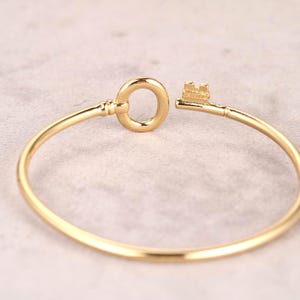 Puede incluir: Un brazalete dorado en forma de llave. El brazalete presenta un dise&ntilde;o de llave en el cierre, con la cabeza y el asa circular de la llave formando el cierre. El brazalete tiene aproximadamente 6,35 cm de di&aacute;metro.