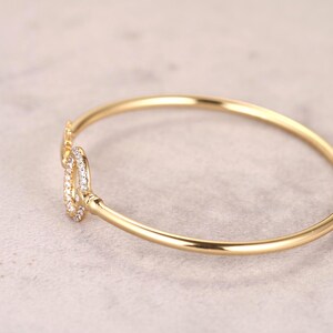 Puede incluir: Un brazalete dorado con un cierre decorativo. El cierre est&aacute; adornado con peque&ntilde;as piedras preciosas transparentes. El brazalete se encuentra sobre un fondo neutro, resaltando su elegante dise&ntilde;o. Una joya.