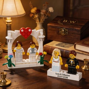 Puede incluir: Dos conjuntos de figuras de bloques de construcción que representan parejas de boda. Un conjunto presenta un arco blanco con un corazón rojo, mientras que el otro se apoya en una base blanca con el texto Luiza & Sebastian 20.07.2026 impreso.
