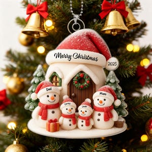 Puede incluir: Adorno navideño con una casa con techo de gorro de Papá Noel y el texto "Merry Christmas". Los muñecos de nieve con bufandas y sombreros rojos representan a una familia. También incluye el año 2025.