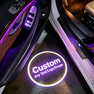 Può includere: Una luce per proiettore da portiera auto che proietta un bagliore circolare bianco e giallo a terra. La proiezione mostra la parola Custom in grandi lettere sopra il testo Any Text/Logo/Image, all'interno di un veicolo con illuminazione.