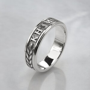 May include: A silver band ring with an engraved inscription that reads "KHS MM" and a wheat design.