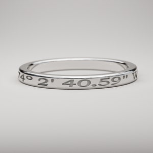 May include: A silver ring with the coordinates "74&deg; 2' 40.59" W" engraved around the band.