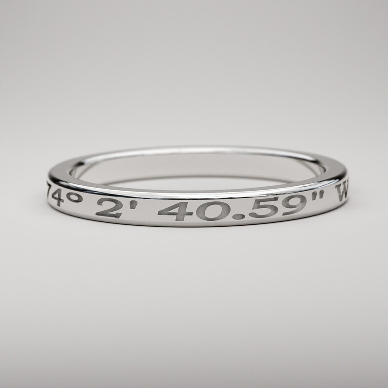 May include: A silver ring with the coordinates "74&deg; 2' 40.59" W" engraved around the band.