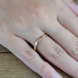 May include: A thin gold band ring with an inscription on the outside of the band.