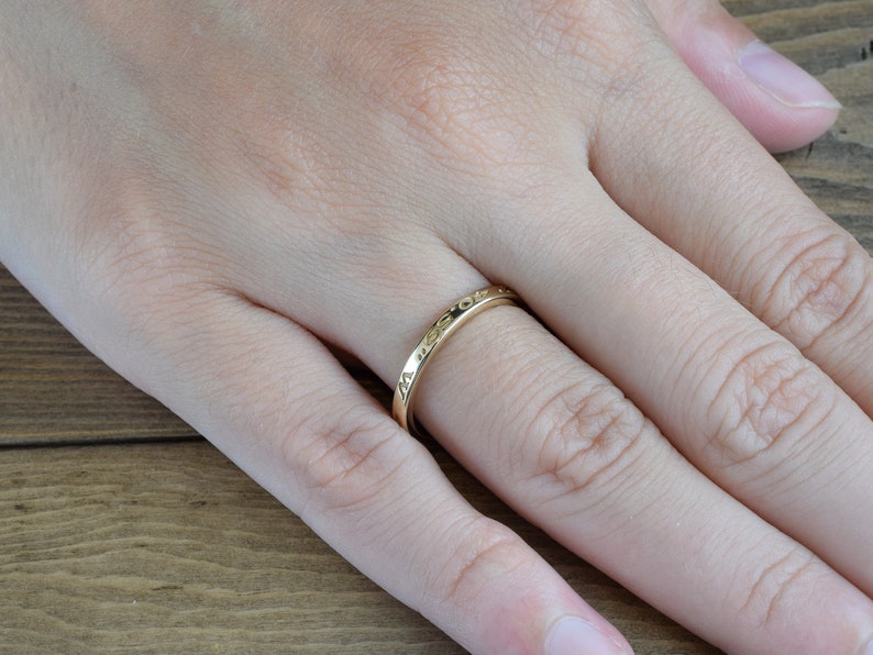 May include: A thin gold band ring with an inscription on the outside of the band.