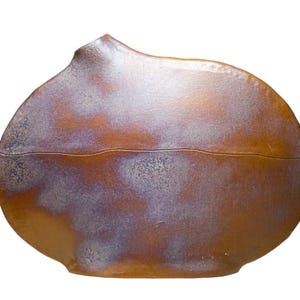 Puede incluir: Un recipiente de cerámica hecho a mano con tapa. El recipiente tiene una forma redondeada con una superficie marrón texturizada y un sutil esmalte púrpura y blanco. La tapa tiene un diseño curvo único.