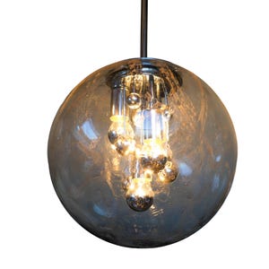 May include: A contemporary pendant light. It features a large, smoky grey glass globe with multiple small, round light bulbs clustered inside. The fixture hangs from a black cord, creating a modern lighting design for a home.