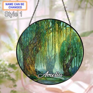 May include: A round, stained-glass window featuring a weeping willow scene in shades of green, yellow, and brown. The name "Amelia" is scripted across the bottom. The window is framed in black and hangs from a chain. Text at the top says "Name can be changed" and "Style 1".