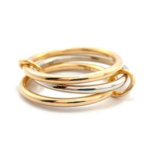 May include: A gold and silver ring set. The ring set features three interlocking bands, with two gold-coloured bands and one silver-coloured band. The bands are smooth and rounded, creating a modern and elegant design.