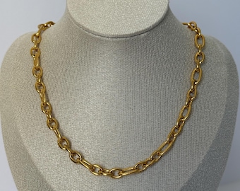 Op de afbeelding: Een goudkleurige ketting bestaande uit een reeks in elkaar grijpende ovale schakels. Het ontwerp wisselt af tussen gladde, gepolijste schakels en getextureerde schakels met een fijn, diagonaal gegraveerd patroon over de gehele lengte.