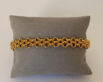 Op de afbeelding: Een goudkleurige kettingarmband met een herhalend patroon van in elkaar grijpende ronde schakels. De armband wordt horizontaal weergegeven en toont een consistente, gepolijste metalen afwerking over de gehele lengte van het ontwerp.