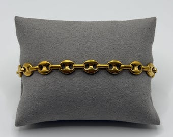 Op de afbeelding: Een goudkleurige armband met een reeks onderling verbonden, afgeronde, ovaalvormige schakels. Het kettingontwerp bestaat uit gladde, gepolijste metaalsegmenten die een uniform, herhalend patroon vormen over de gehele lengte van het sieraad.