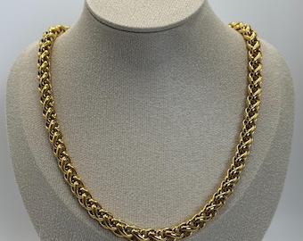 Op de afbeelding: Een goudkleurige ketting met een dik, geweven schakelontwerp in tarwestijl. De ketting heeft een gepolijst, reflecterend oppervlak en een uniform, doorlopend patroon over de gehele lengte van de ketting, wat zorgt voor een robuuste uitstraling.
