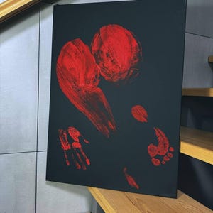 Könnte beinhalten: Abstrakte Kunstleinwand mit roten Hand- und Fußabdrücken auf schwarzem Hintergrund. Das Kunstwerk zeigt kräftige Pinselstriche und ein minimalistisches Design, das einen auffälligen visuellen Kontrast erzeugt. Die Leinwand wird auf einer Holztreppe ausgestellt.