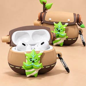 Puede incluir: Dos fundas de silicona para auriculares con forma de bolso marr&oacute;n y un personaje de hoja verde en el frente. Una funda est&aacute; abierta y muestra auriculares inal&aacute;mbricos blancos. Cada funda tiene una base marr&oacute;n oscuro y un mosquet&oacute;n de metal.