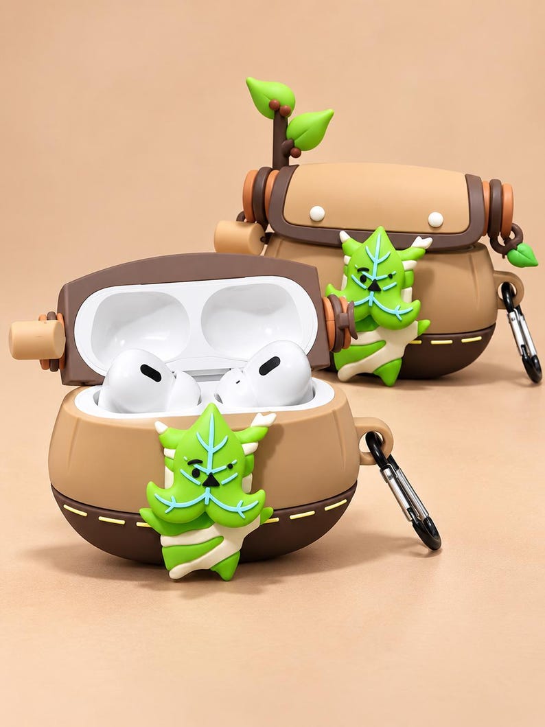 Puede incluir: Dos fundas de silicona para auriculares con forma de bolso marr&oacute;n y un personaje de hoja verde en el frente. Una funda est&aacute; abierta y muestra auriculares inal&aacute;mbricos blancos. Cada funda tiene una base marr&oacute;n oscuro y un mosquet&oacute;n de metal.