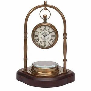 Könnte beinhalten: Eine Tischuhr im Vintage-Stil mit Messing-Finish. Das Zifferblatt ist weiß mit schwarzen römischen Ziffern und Zeigern und trägt den Text "VICTORIA LONDON" und einen Anker. Sie steht auf einem Holzsockel mit einer Lupe.