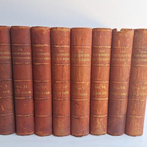 May include: A set of eight antique books titled The Harmsworth Encyclopedia, volumes I through VIII. Each book features a weathered, textured brown leather spine with gold embossed lettering and horizontal decorative lines along the spine.