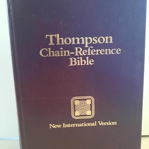 May include: A dark purple Thompson Chain-Reference Bible with gold lettering. The cover features the title, a cross symbol, and "New International Version". The book has a gradient effect from dark purple to a lighter shade.