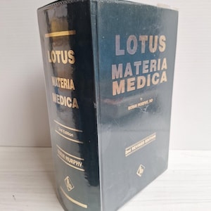 Può includere: Un libro con copertina rigida verde scuro intitolato Lotus Materia Medica, 2nd Revised Edition di Robin Murphy, ND. La copertina e il dorso presentano scritte dorate e un piccolo logo in basso. Il libro è posizionato in verticale.