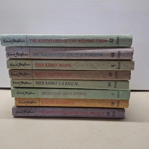 以下が含まれることがあります： エニッド・ブライトンの児童書が積み重ねられています。「The Adventures of the Wishing Chair」や「Brer Rabbit Again」などのタイトルがあります。本はカラフルな背表紙で、互いの上に積み重ねられています。