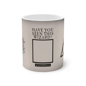 Può includere: Una tazza in ceramica beige con la scritta "HAVE YOU SEEN THIS WIZARD?" in nero. La tazza presenta un telaio nero, un fulmine e altri elementi grafici. Il fondo della tazza ha un messaggio di avvertimento.