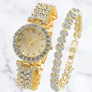 May include: A gold watch and bracelet set. The watch has a round face with crystal detailing and a gold strap. The bracelet has a matching design with crystal embellishments. The watch face displays the numbers 1 to 12.