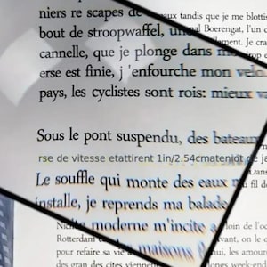 Può includere: Una lente d'ingrandimento con montatura nera è posizionata su una pagina stampata. Il testo è nero su sfondo bianco. La lente viene utilizzata per ingrandire il testo, facilitando la lettura. L'immagine è ben illuminata e nitida.