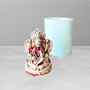 May include: A detailed cream-colored statue with red accents depicts a seated figure with ornate details. Beside it is a light blue cylindrical object. The statue is likely a religious or decorative item.