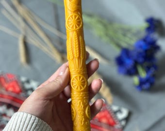 May include: A tall, yellow beeswax candle with intricate embossed designs. The candle features a dove, wheat stalks, and geometric patterns. The candle is approximately 8 inches tall and is a decorative item.