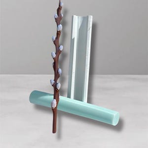 Könnte beinhalten: Eine braune, zweigartige Skulptur mit weißen und hellvioletten Akzenten, positioniert mit einem hellblauen Zylinder und einem weißen, rechteckigen Objekt. Die Objekte sind vor einem hellgrauen Hintergrund angeordnet.