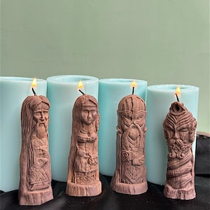 May include: Four brown, carved candles depicting Viking figures, each with a lit wick. The candles are in front of light blue cylindrical molds. The carvings feature detailed faces, beards, and symbols, creating a rustic and thematic aesthetic.