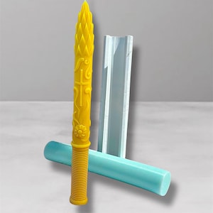 Peut inclure: Une bougie jaune sculptée avec une croix et un motif floral, à côté d'un moule bleu clair. La bougie a une base texturée et nervurée et un sommet pointu. Le moule est rectangulaire et cylindrique.