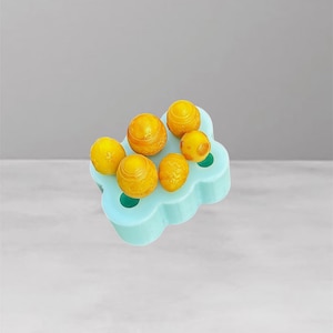 May include: A light blue silicone mould holding six yellow spheres. The spheres have a textured surface and appear to be food items. The mould has a cloud-like shape with circular indentations.