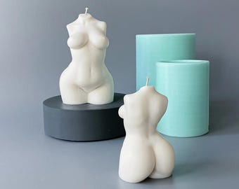 May include: Off-white, body-shaped candles with wicks, displayed on a gray surface. One candle is on a dark gray pedestal. Two cylindrical, light blue candles are in the background. The candles are a decorative home decor item.