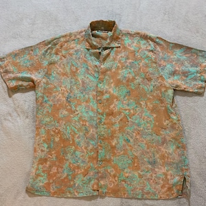 Peut inclure: Chemise à manches courtes avec un motif cachemire dans les tons marron, turquoise et bleu. La chemise a un col classique et une fermeture boutonnée. Le tissu semble léger.