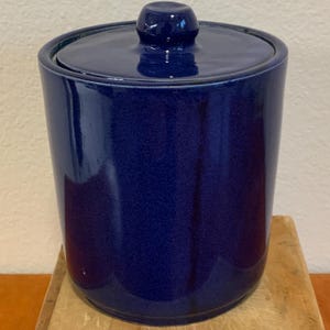 Op de afbeelding: Een kobaltblauwe keramische pot met bijpassende deksel. De pot is cilindrisch met een licht getextureerd oppervlak en een glanzende afwerking. De deksel heeft een kleine, afgeronde knop. De pot is ongeveer 15 cm hoog.