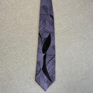 Könnte beinhalten: Eine lavendelfarbene Krawatte mit einem schwarzen, abstrakten Design. Die Krawatte hat ein sich wiederholendes Muster aus kleinen Punkten und geschwungenen Linien in Schwarz und Türkis. Die Krawatte ist aus glattem Stoff und für formelle Anlässe geeignet.