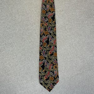 May include: A necktie featuring a black background with a dense, repeating pattern of paisley shapes and floral motifs in shades of gold, olive green, red, and blue. The tie has a pointed tip and a standard tapered shape with a smooth, woven texture.