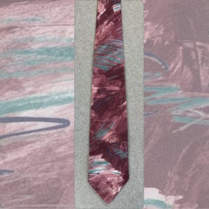 May include: A necktie featuring a deep maroon base color with an abstract pattern of brushstroke-like markings in shades of teal, light pink, and dark blue. The design consists of layered, diagonal, and circular strokes across the fabric surface.