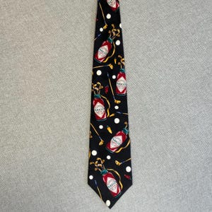 Può includere: Cravatta nera con un motivo ripetuto di bottiglie di salsa Tabasco, mazze da golf e pois bianchi. Le bottiglie di Tabasco sono rosse con etichette bianche. Le mazze da golf sono dorate e i pois bianchi.