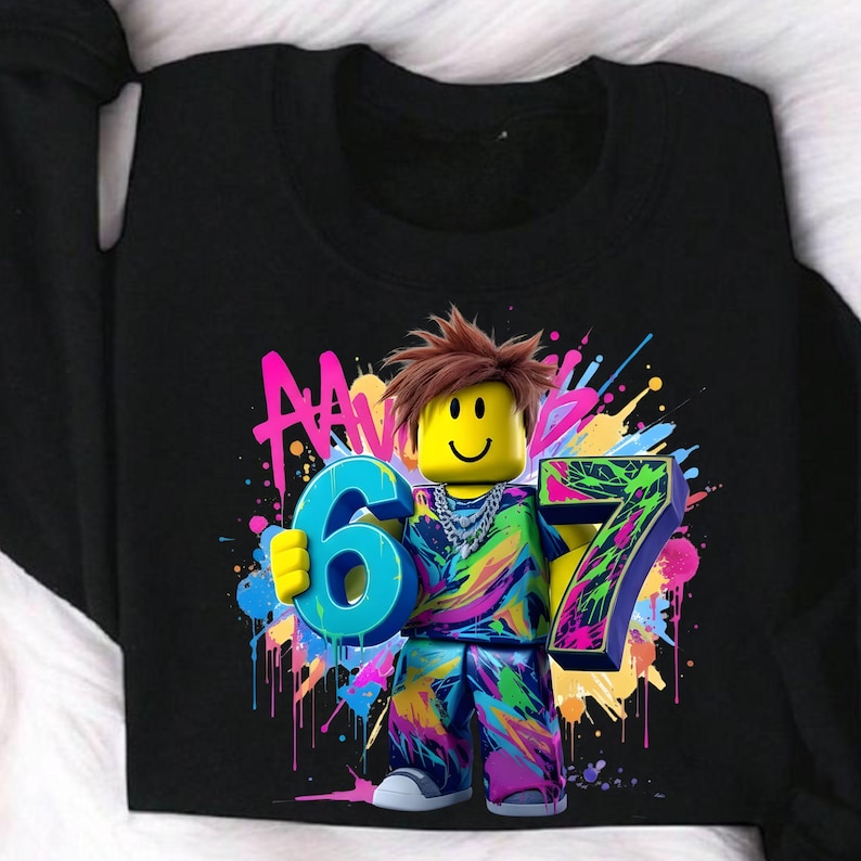 May include: Black sweatshirt featuring a colorful graphic of a block figure holding the numbers 6 and 7. The figure has brown hair and a smiling face. The background has colorful paint splatters and the word "AAN".